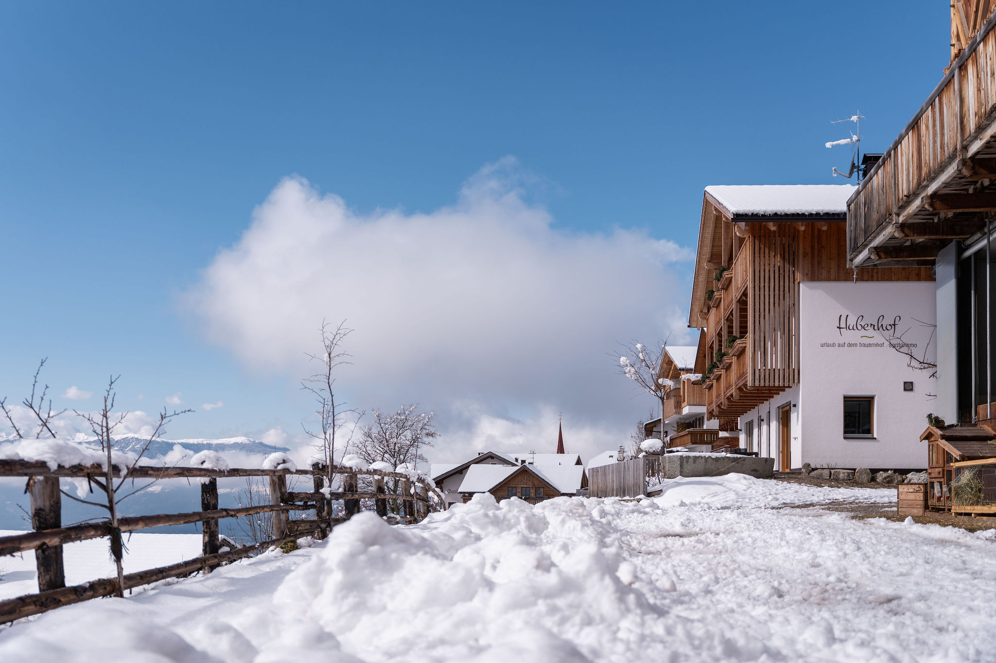 Der Huberhof im Winter mit verschneitem Hofplatz und blauem Himmel