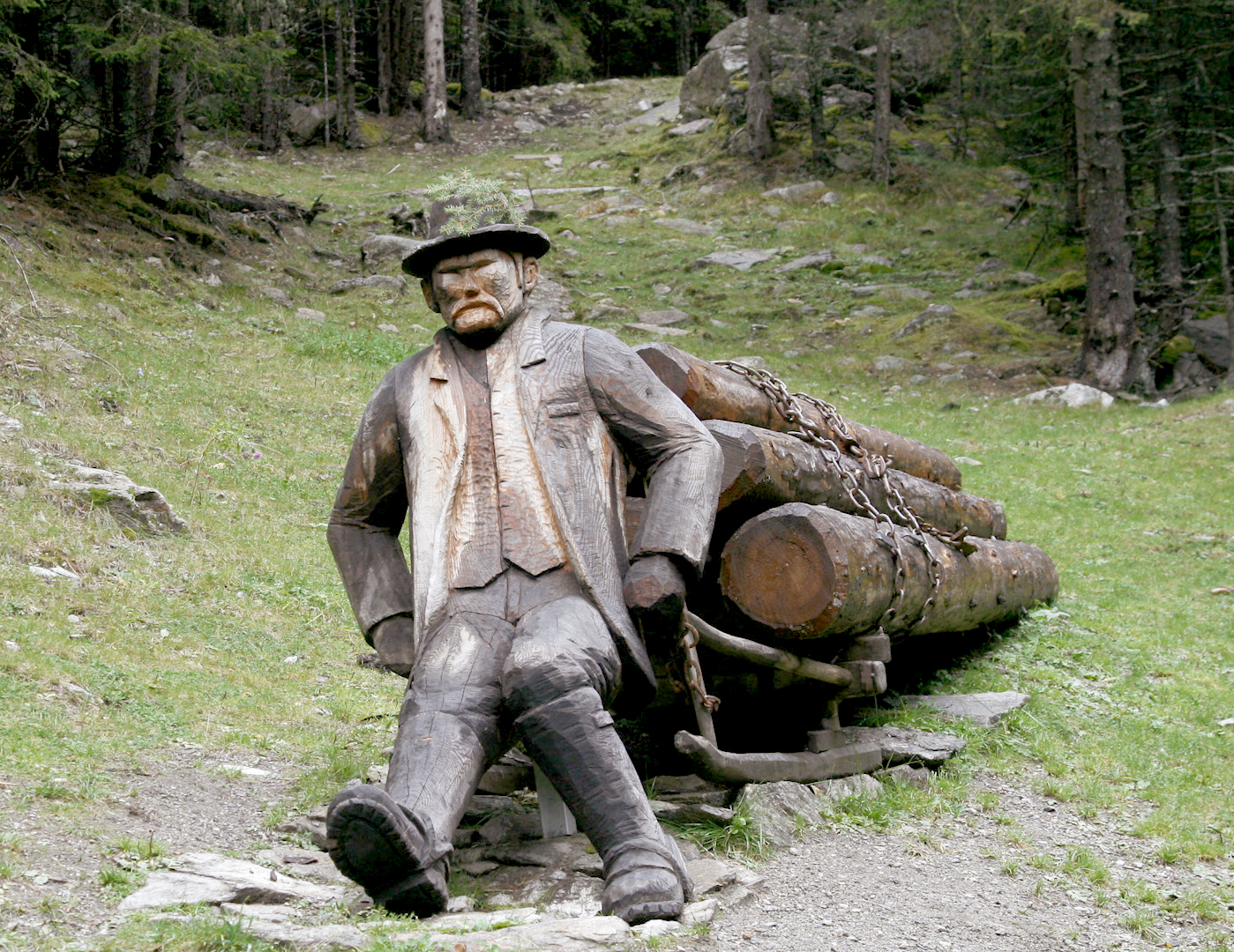 Wooden sculpture of a man resting by a pile of logs on the nature trail in the Mühlbacher Talile